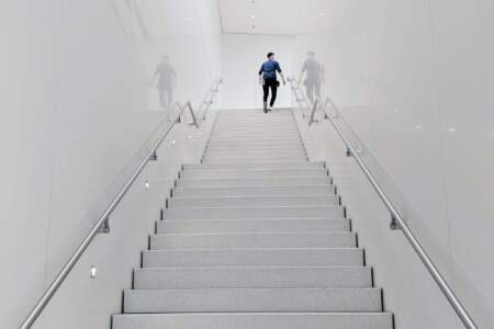 Person geht in einem weißen Gebäude eine breite Treppe hinauf