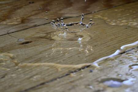 Wassertropfen spritzt auf nassem Holzboden – Symbolbild für Wasserschaden